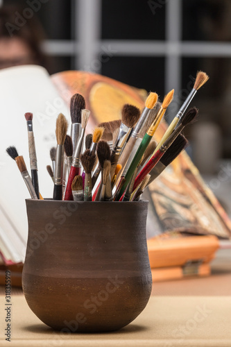 various brushes in a ceramic container, in the background an open book