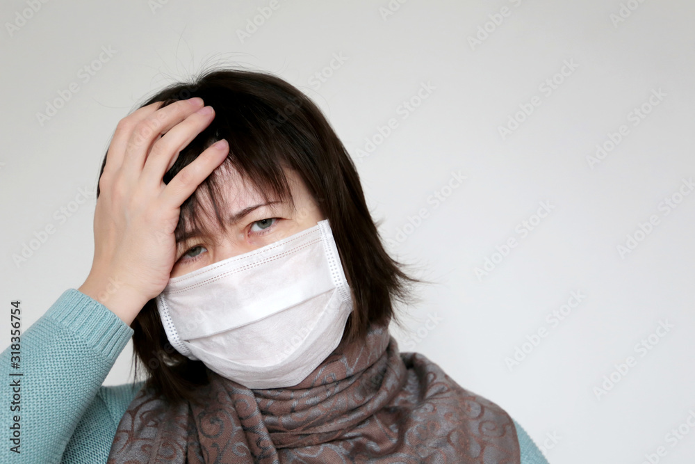 Unhappy woman in medical mask holds hand to her forehead. Concept of illness, fever, cold and flu, head pain, coronavirus symptoms