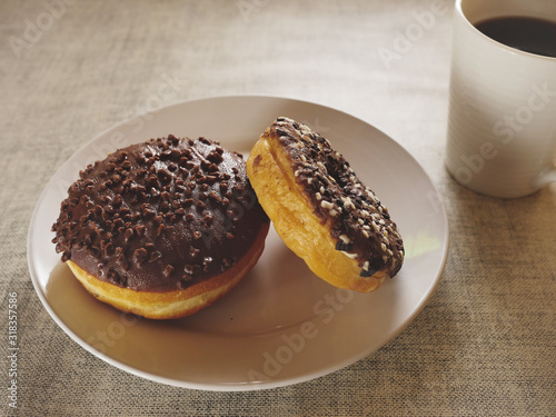 Two chocolate doughnut on a white plate and a cup of tea on a simple table cloth, Concept break, breakfast.