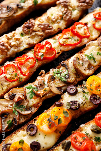 Vegetarian toasts with mozzarella cheese, various toppings sprinkled with herbs on the black background, top view, close up.