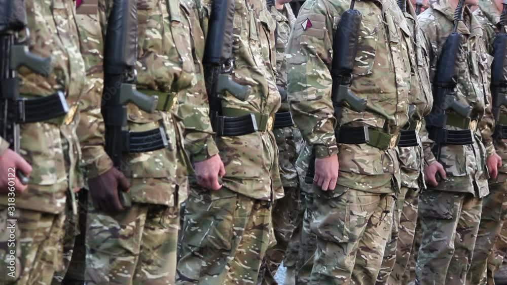 Army Soldiers parade stood in formation with guns in camouflage. They are performing drills