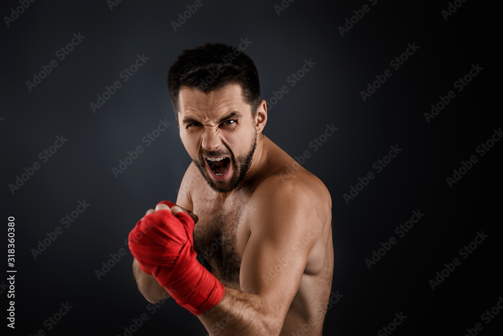 Sportsman boxer throwing a fierce and powerful punch. muscular man with red bandage on hands on black background.