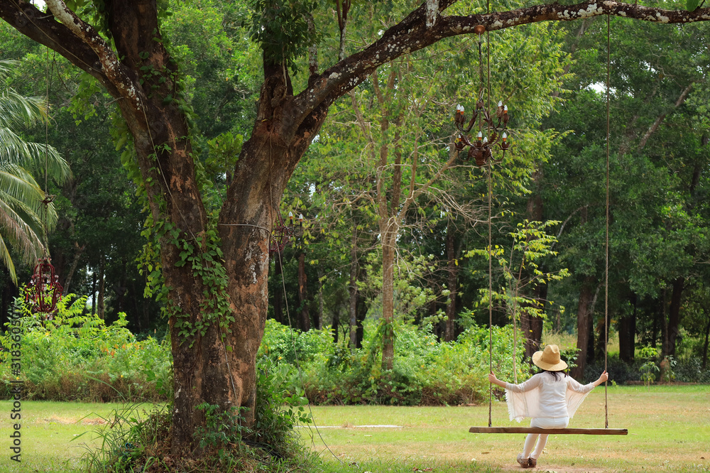 Woman relaxing on wooden swing under the big tree in the park Woman relaxing on wooden swing under the big tree in the park