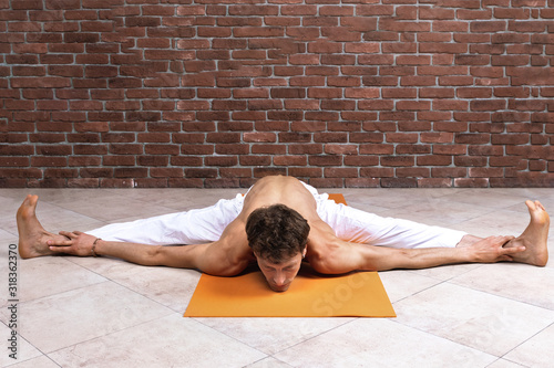 Sporty man practicing hatha yoga in studio. Male in white pants sitting in Wide-Angle Forward Bend pose, Upavishtha Konasana. Yogi, sport and healthy concept with copy space photo