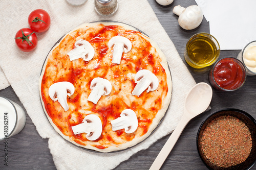 Pizza with mushrooms on a wooden table, on the background of ingredients for it, spices, olive oil, tomatoes and mushrooms. The concept of making pizza.