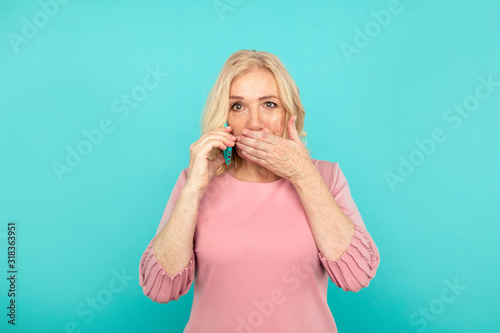 Mid blond woman with phone closing her mouth isolated