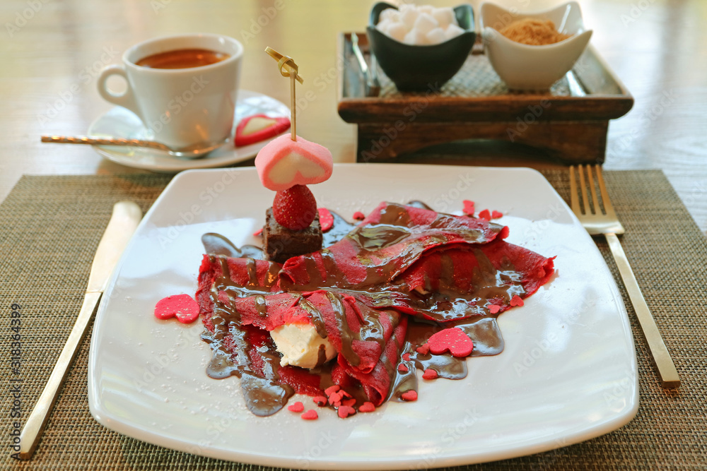 Raspberry red crepe with chocolate sauce and pink heart shaped candies served with a cup of coffee Raspberry red crepe with chocolate sauce and pink heart shaped candies served with a cup of coffee