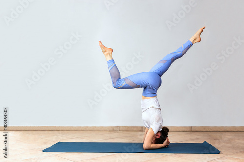 Yogi girl standing in Adho Mukha Vrksasana exercise. Woman in headstand practicing at yoga studio. Downward facing Tree Pose, copy space