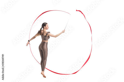 Slender graceful girl gymnast in beige sportswear dancing with a red developing ribbon isolated on a white background.