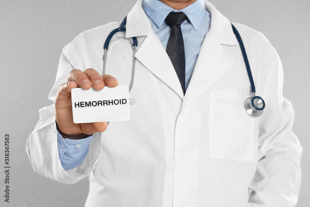 Doctor holding business card with word HEMORRHOID on light grey background, closeup Doctor holding business card with word HEMORRHOID on light grey background, closeup