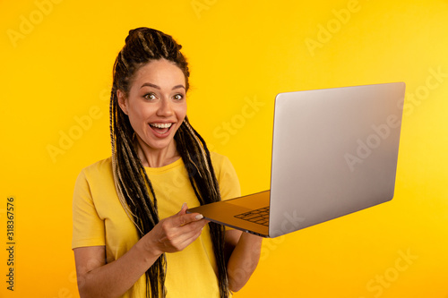 Portrait of happy exited young lady with laptop isolated over the yellow studio