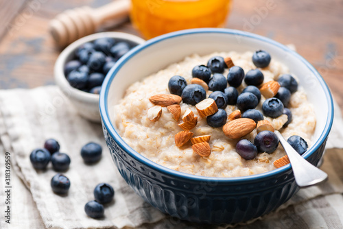 Fototapete Oatmeal with blueberries and almonds in blue ceramic bowl on a wooden table