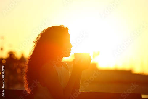 Silhouette of a woman holding coffee mug at sunset