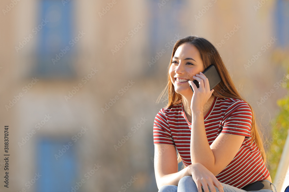 Happy girl talking on mobile phone sitting outdoors - obrazy, fototapety, plakaty 