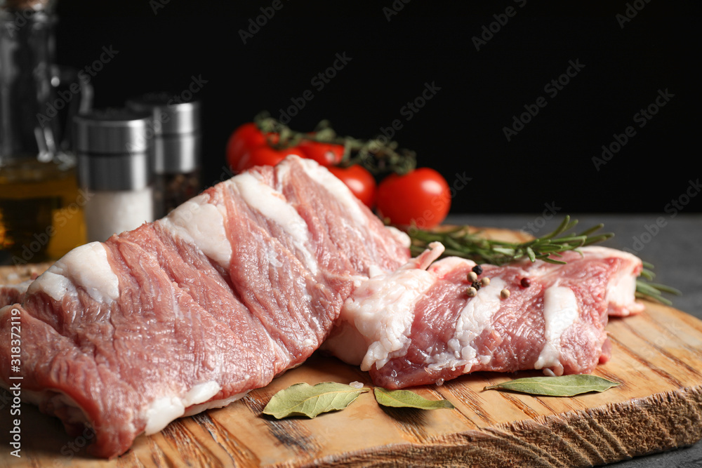 Raw ribs with bay leaves and pepper on wooden board, closeup