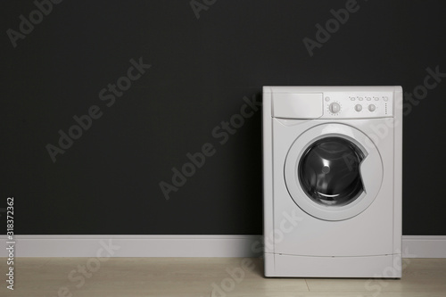 Modern washing machine near black wall, space for text. Laundry day