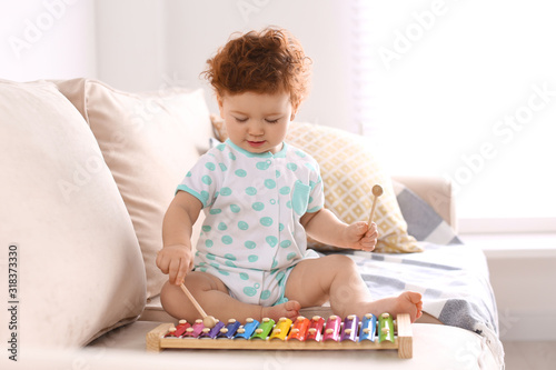 Cute little child playing with xylophone on sofa at home