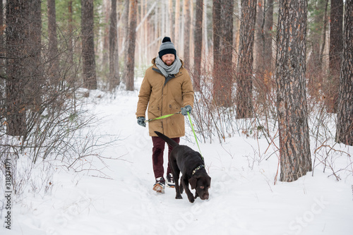 Happy young man in winterwear holding leash of black retriever during chill