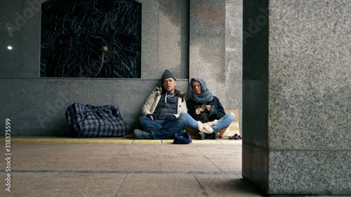 homeless people ask for alms sitting on the sidewalk against the wall