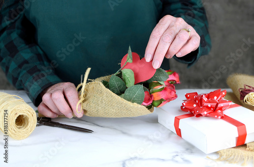 people, shopping, sale, florist, valentine's day and consumerism concept - close up of causcasian florist woman wrapping red rosebuds in burlap at flower shop photo