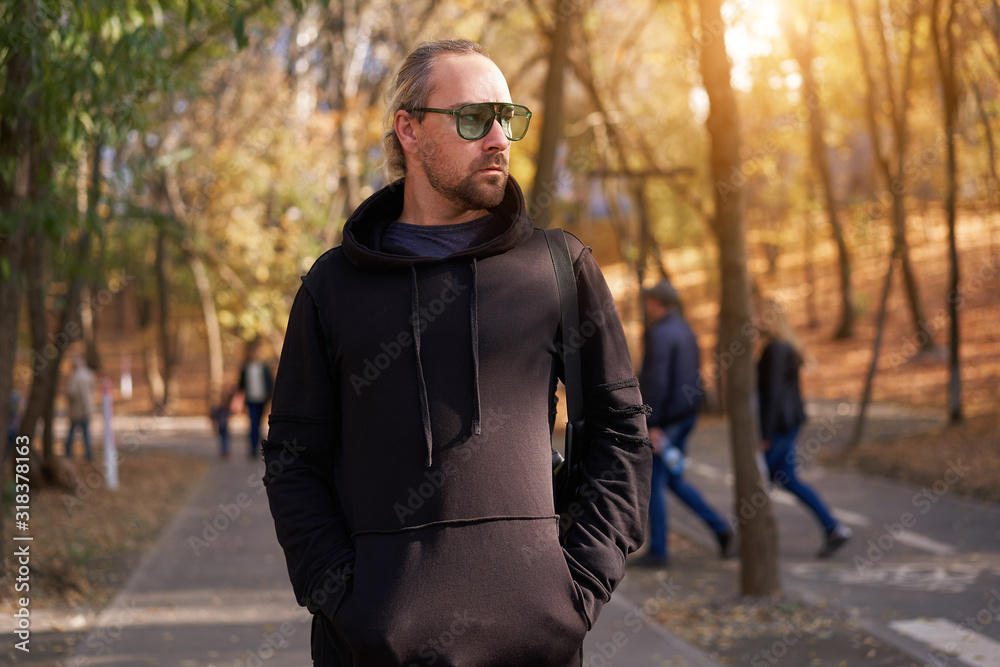 Handsome young unshaven man black hoodie and sunglasses walking autumn park warm day. Handsome young unshaven man black hoodie and sunglasses walking autumn park warm day.