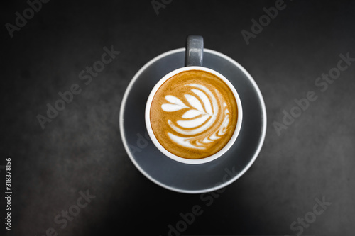 Gray cup of fresh cappuccino with latte art on dark black metal table background. Empty place for text, copy space. Coffee addiction concept. Top view from above.