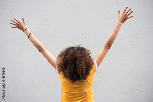 behind of young woman with curly hair and arms raised by gray background