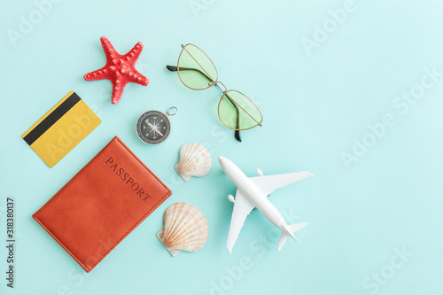 Vacation travel adventure trip concept. Minimal simple flat lay with plane passport sunglasses compass gold credit card shell on blue pastel colourful trendy background. Tourist essentials