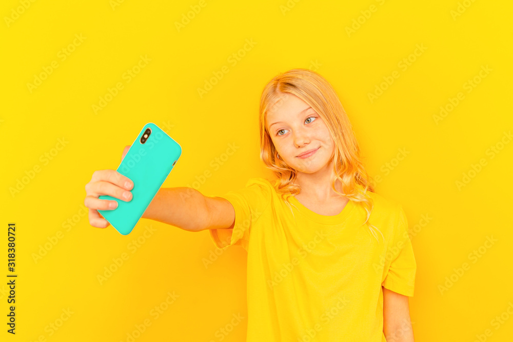 Smiling little girl kid showing blue screen of new popular mobile phone on light yellow background Smiling little girl kid showing blue screen of new popular mobile phone on light yellow background