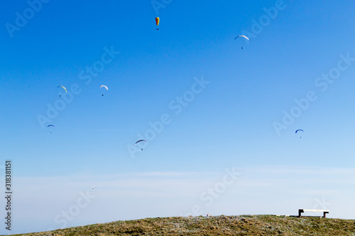 Paraglider on blue sky with empty bench on foreground