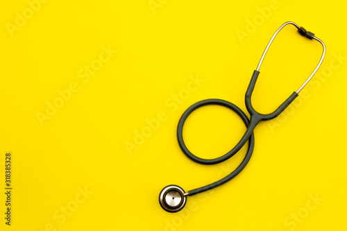 Above shot of a stethoscope puts on the left side of a table on a yellow background.