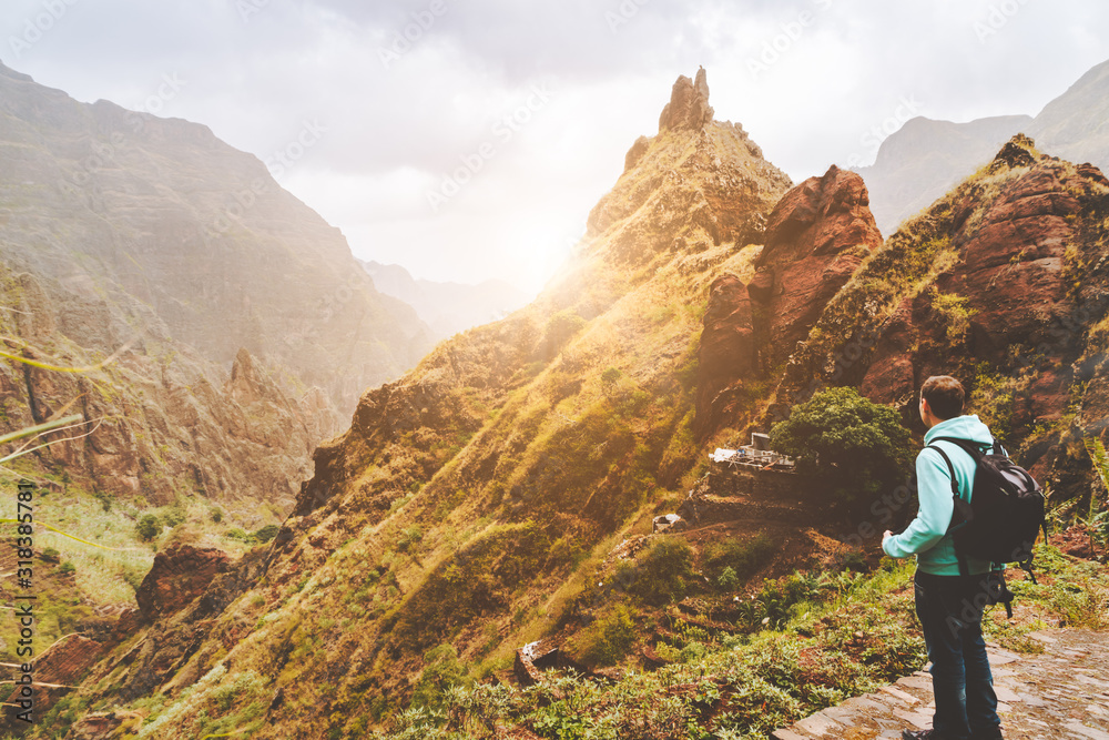 Naklejka premium Santo Antao Island, Cape Verde. Traveler man with camera on sunset in front of mountain ridge and ravine on the cobbled path to Xo-Xo Valley