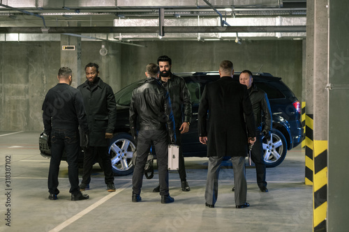 Several intercultural men in black discussing terms of criminal business photo