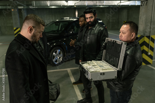 Mature man in black jacket, gloves and jeans opening suitcase with dollars photo