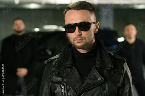 Criminal authority in sunglasses and leather jacket standing on parking area © pressmaster