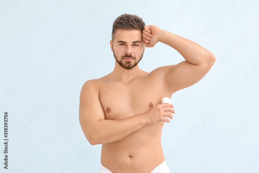 Handsome young man using deodorant on color background