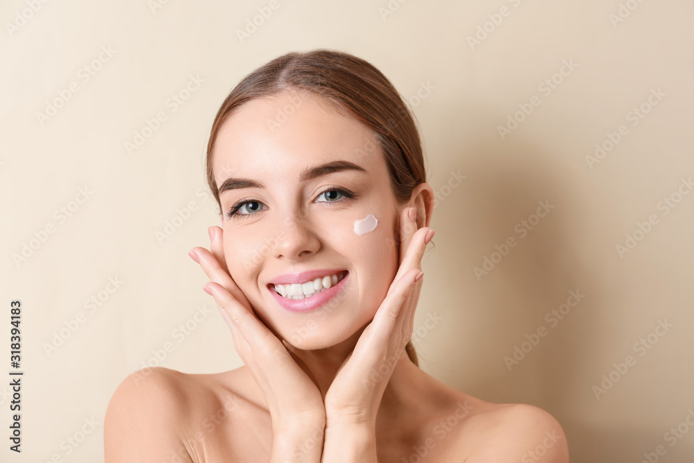 Beautiful young woman applying cream on her face against color background Beautiful young woman applying cream on her face against color background