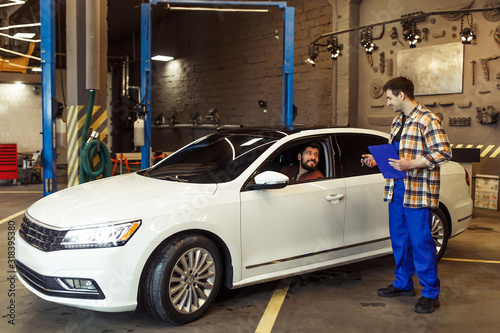 male client talking with technician and leaving modern auto service center on luxury car after repairing