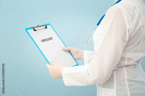 Female urologist with clipboard on color background, closeup