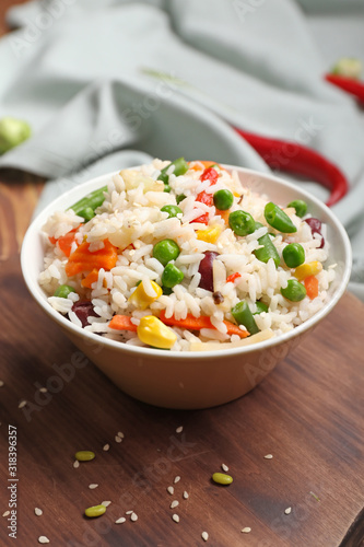 Bowl with boiled rice and vegetables on table