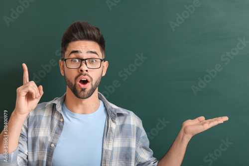 Male teacher with raised index finger near blackboard in classroom