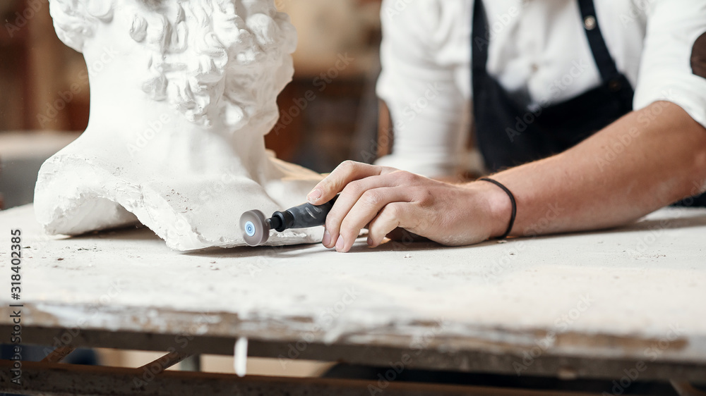 Obraz premium Male sculptor repairing gypsum sculpture of woman's head at the working place in the creative artistic studio.