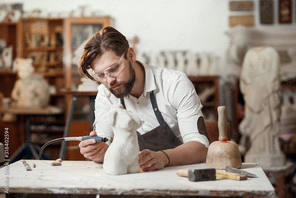 Male sculptor repairing gypsum sculpture of woman's head at the working place in the creative artistic studio. Male sculptor repairing gypsum sculpture of woman's head at the working place in the creative artistic studio.