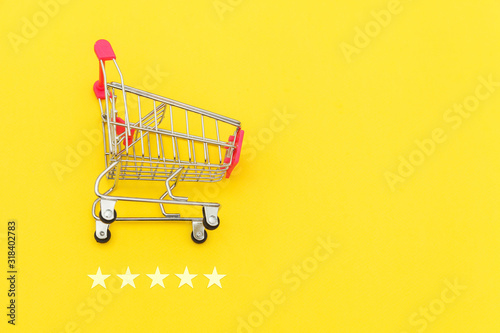 Small supermarket grocery push cart for shopping toy with wheels and 5 stars rating isolated on yellow background. Retail consumer buying online assessment and review concept.