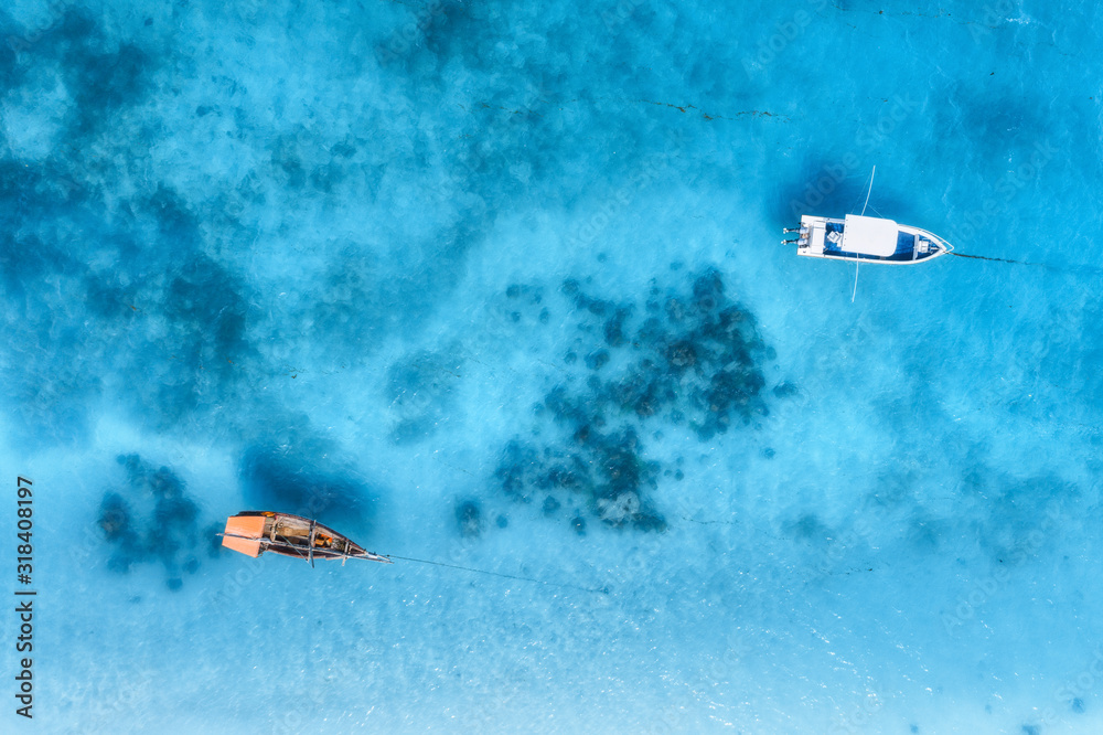Aerial view of the fishing boat and yacht in clear blue sea at sunset in summer. Top view from drone of yachts, sandy beach. Travel in Zanzibar, Africa. Tropical landscape with motorboat, water Aerial view of the fishing boat and yacht in clear blue sea at sunset in summer. Top view from drone of yachts, sandy beach. Travel in Zanzibar, Africa. Tropical landscape with motorboat, water