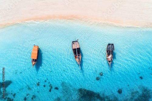 Aerial view of the fishing boats in clear blue water at sunset in summer. Top view from drone of boat, yacht, sandy beach in Zanzibar. Travel. Tropical seascape with sailboats, sea. View from above