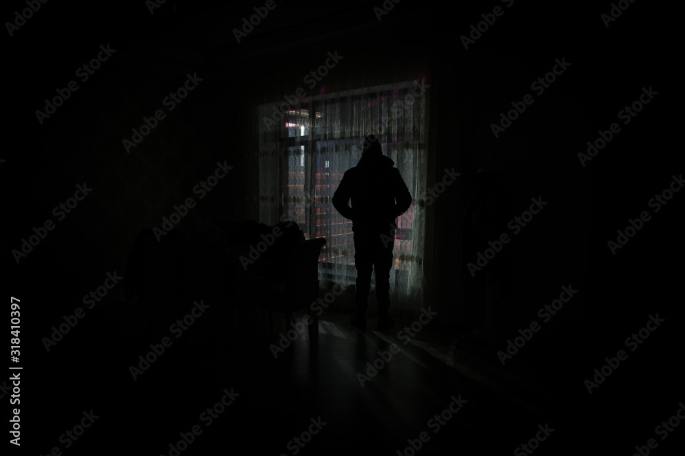 Silhouette of a man standing at a window inside the room. Fantasy picture with old vintage lantern at the window inside dark room.