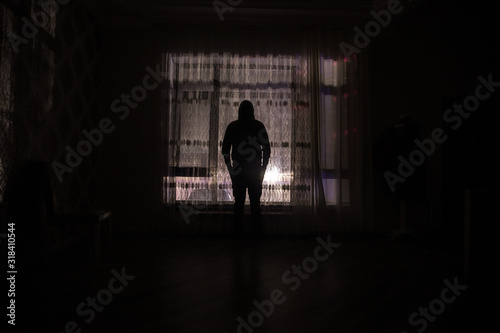Silhouette of a man standing at a window inside the room. Fantasy picture with old vintage lantern at the window inside dark room.