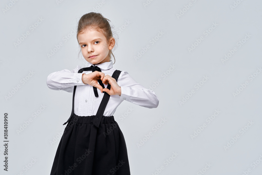 Portrait of nice attractive lovely charming cute kind cheerful cheery careful pre-teen girl in school uniform showing heart gesture isolated over grey color background. Portrait of nice attractive lovely charming cute kind cheerful cheery careful pre-teen girl in school uniform showing heart gesture isolated over grey color background.