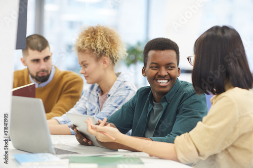 Multi-ethnic group of students studying in college library, focus on African-American man smiling at partner © Seventyfour